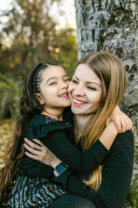 A mother and daughter share a loving embrace outdoors on a bright autumn day.