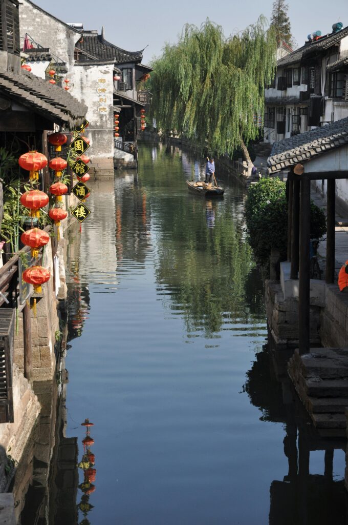 Picturesque view of a traditional Chinese canal with red lanterns and a person rowing a boat.