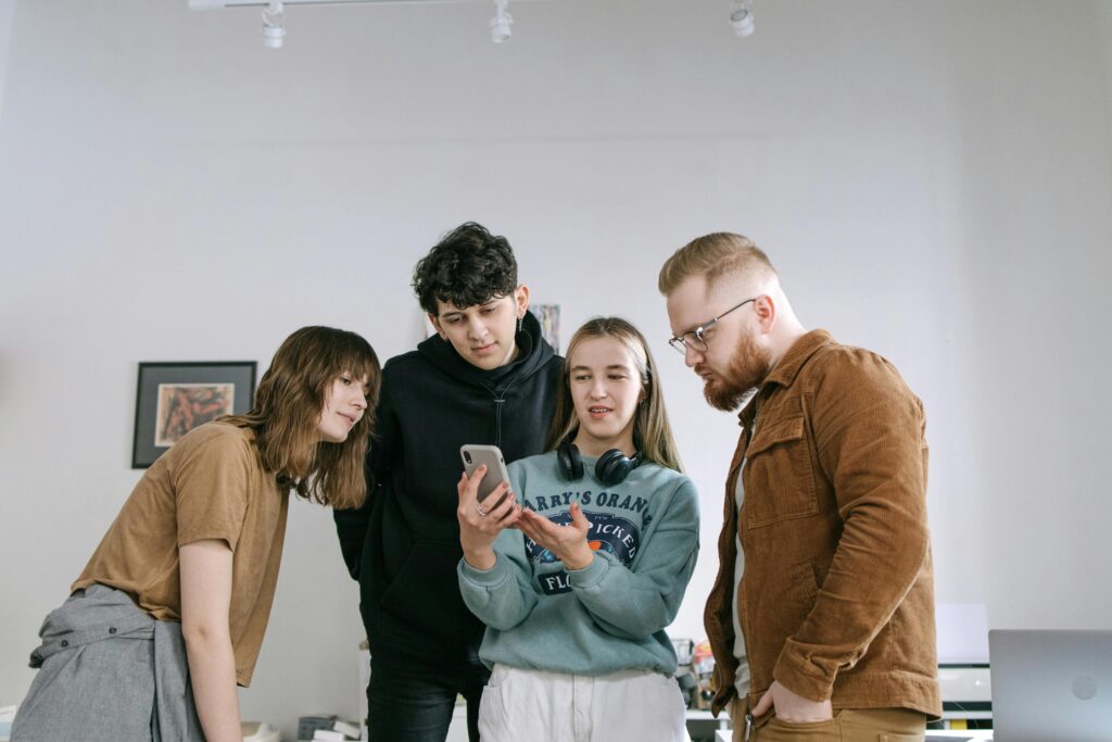 Group of young adults reviewing content on a smartphone in an office setting.